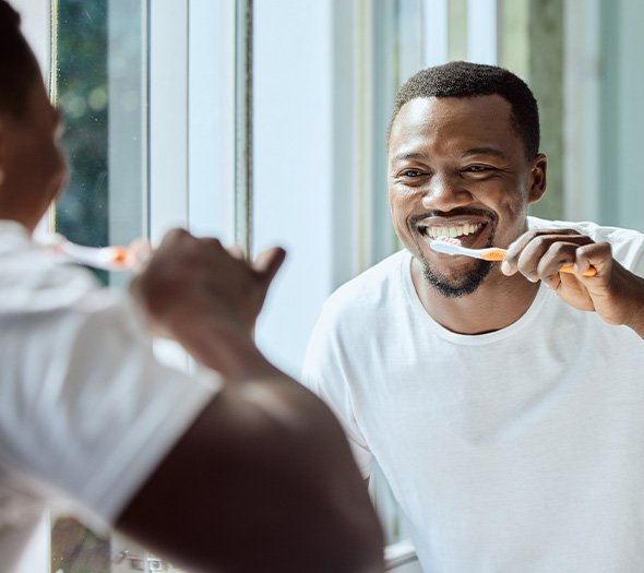 Man smiling while brushing his teeth