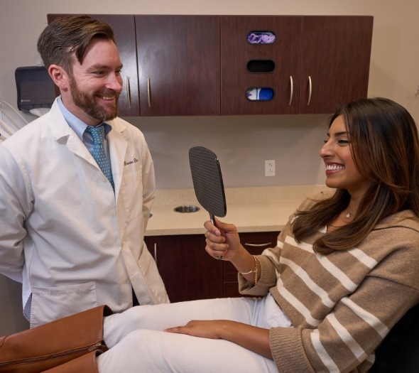 Male dentist watching female patient check teeth