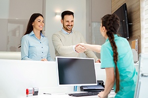 A couple shakes hands with a dental receptionist who is preparing to go over their dental insurance plan 