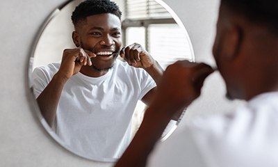 Man smiling while flossing in bathroom