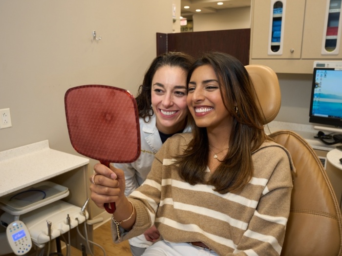 Female patient and dentist smiling at mirror together