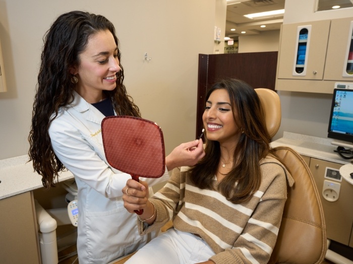 Female dentist watching patient check smile in mirror