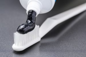 A tube of charcoal toothpaste being squeezed onto a toothbrush.