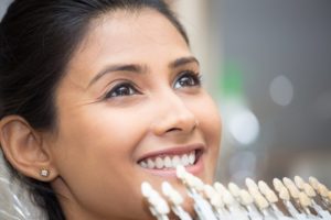 a dentist using a shade guide on a female patient’s teeth