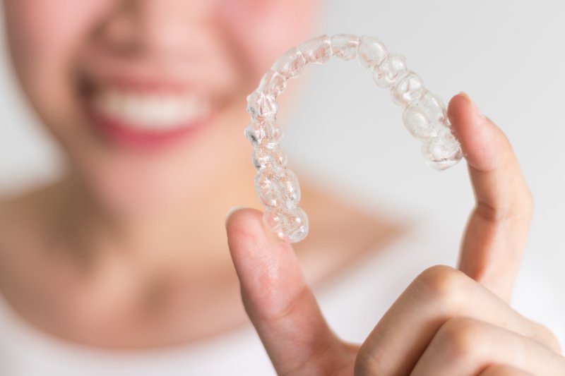 Woman smiling while holding Invisalign tray