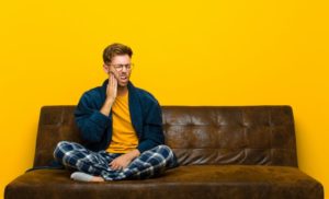 a man sitting on his couch in his pajamas having a severe toothache 