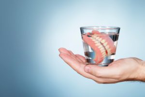 Hand holding a glass of clear liquid with dentures